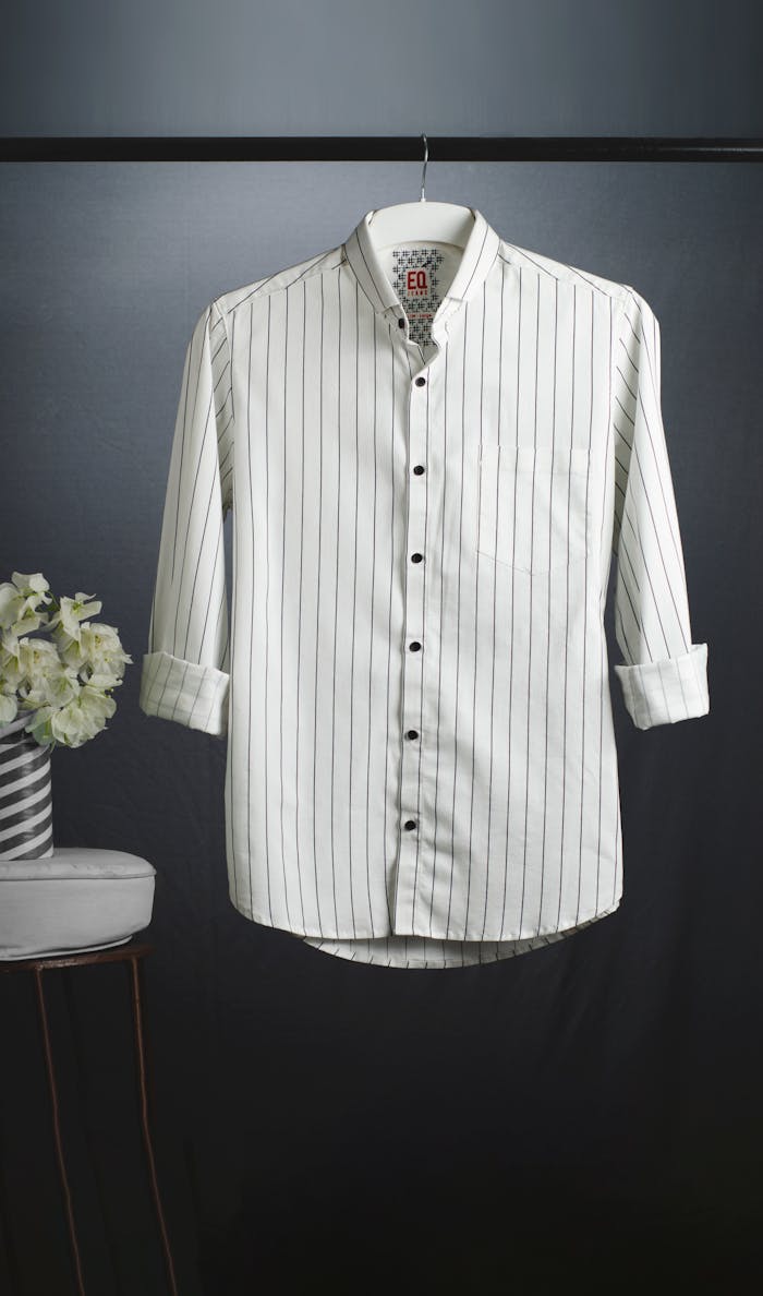 Stylish white striped shirt hanging elegantly in a studio setting next to a floral arrangement.
