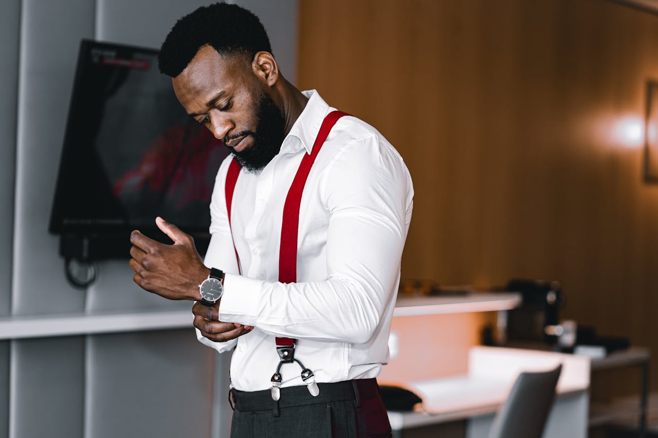 Elegant man in red suspenders adjusts cufflinks, preparing for a formal occasion.